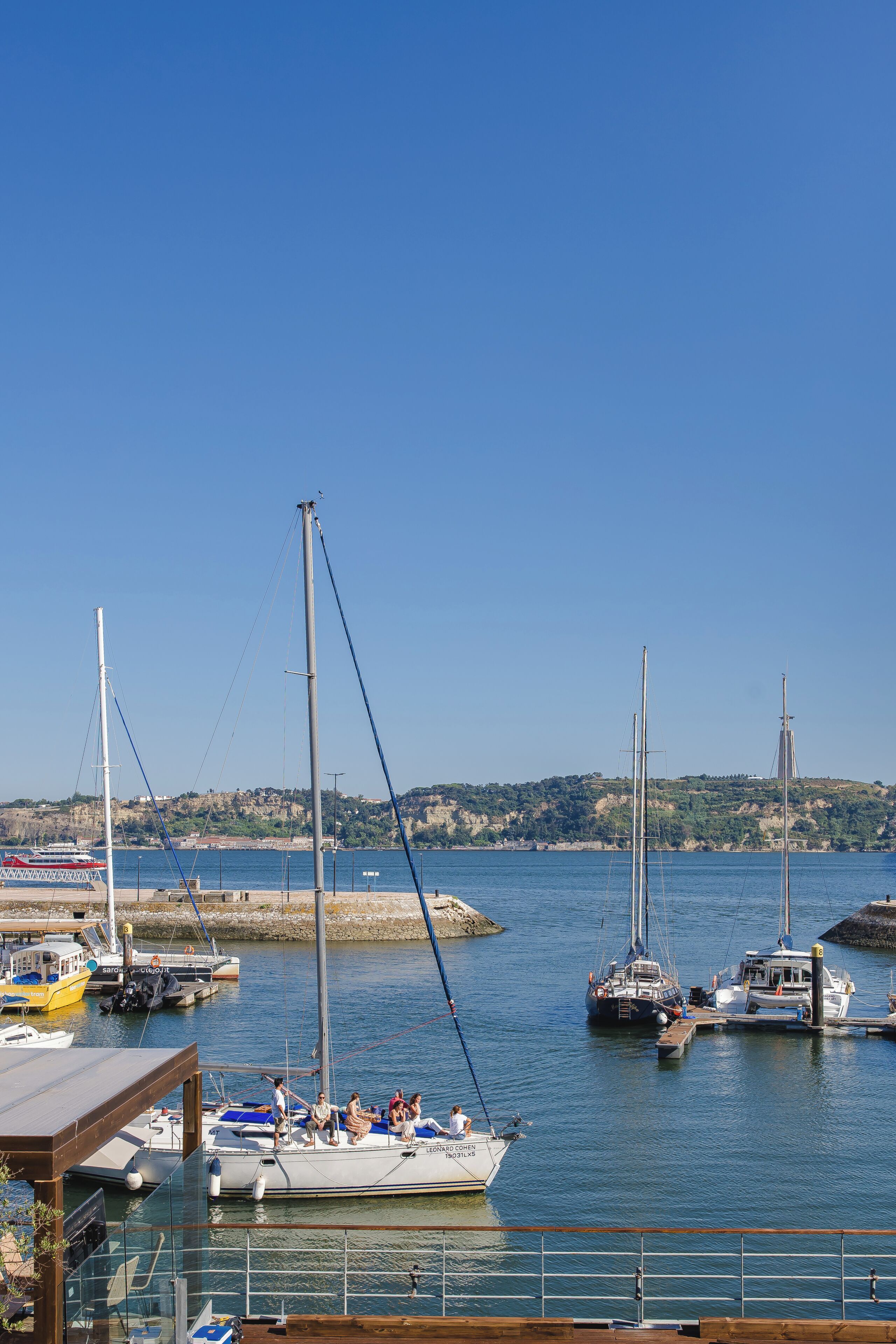 Una marina con barcos amarrados, cielo despejado y un paisaje montañoso al fondo.