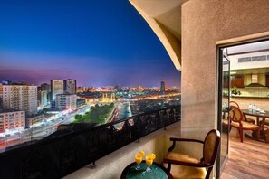 Un balcon avec vue sur la ville, une table avec deux boissons et un coin repas avec des chaises et une table.