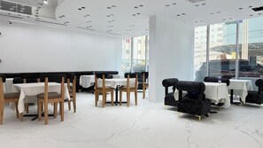 A modern restaurant interior with white walls, marble flooring, and a mix of wooden and upholstered chairs. - Palette Sharjah Aparthotel Formerly Royal Tulip (Sharjah)