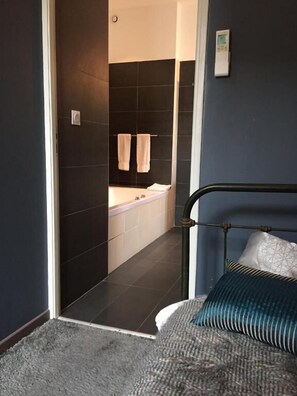 Un dormitorio con cama, cabecera y vista al baño.