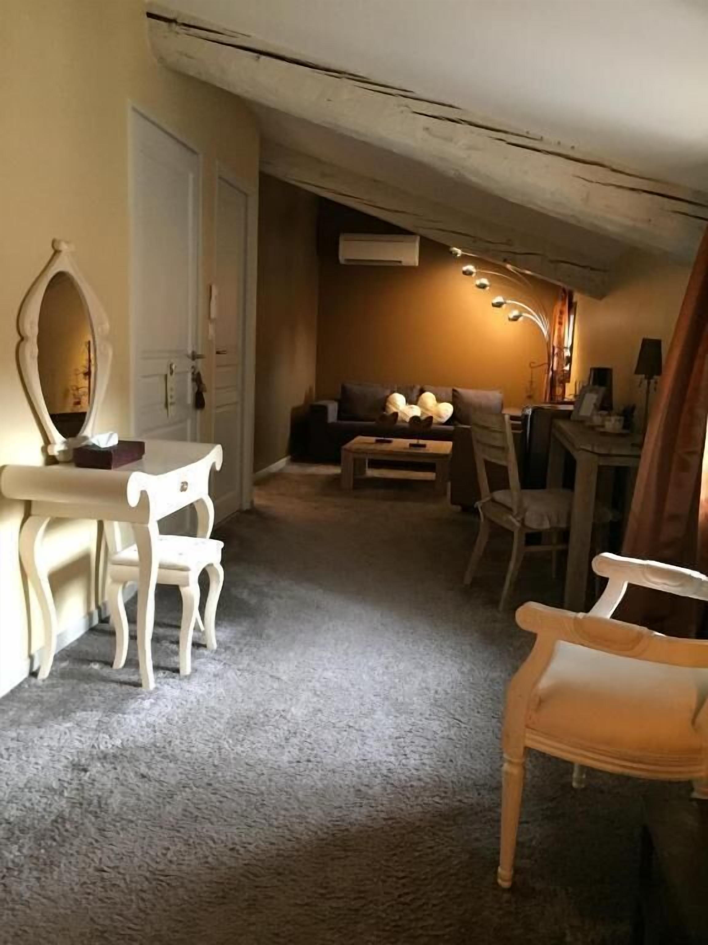 Una habitación con un escritorio blanco, una silla, un sofá y un espejo. Se ve una puerta y un aplique en el techo.