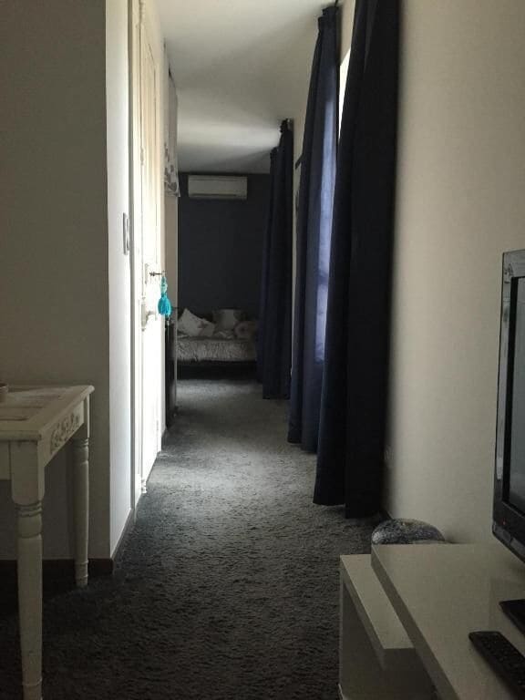Un couloir étroit, avec un lit au fond, une télévision sur le côté droit et une porte sur le côté gauche.