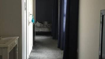 Un couloir étroit, avec un lit au fond, une télévision sur le côté droit et une porte sur le côté gauche.