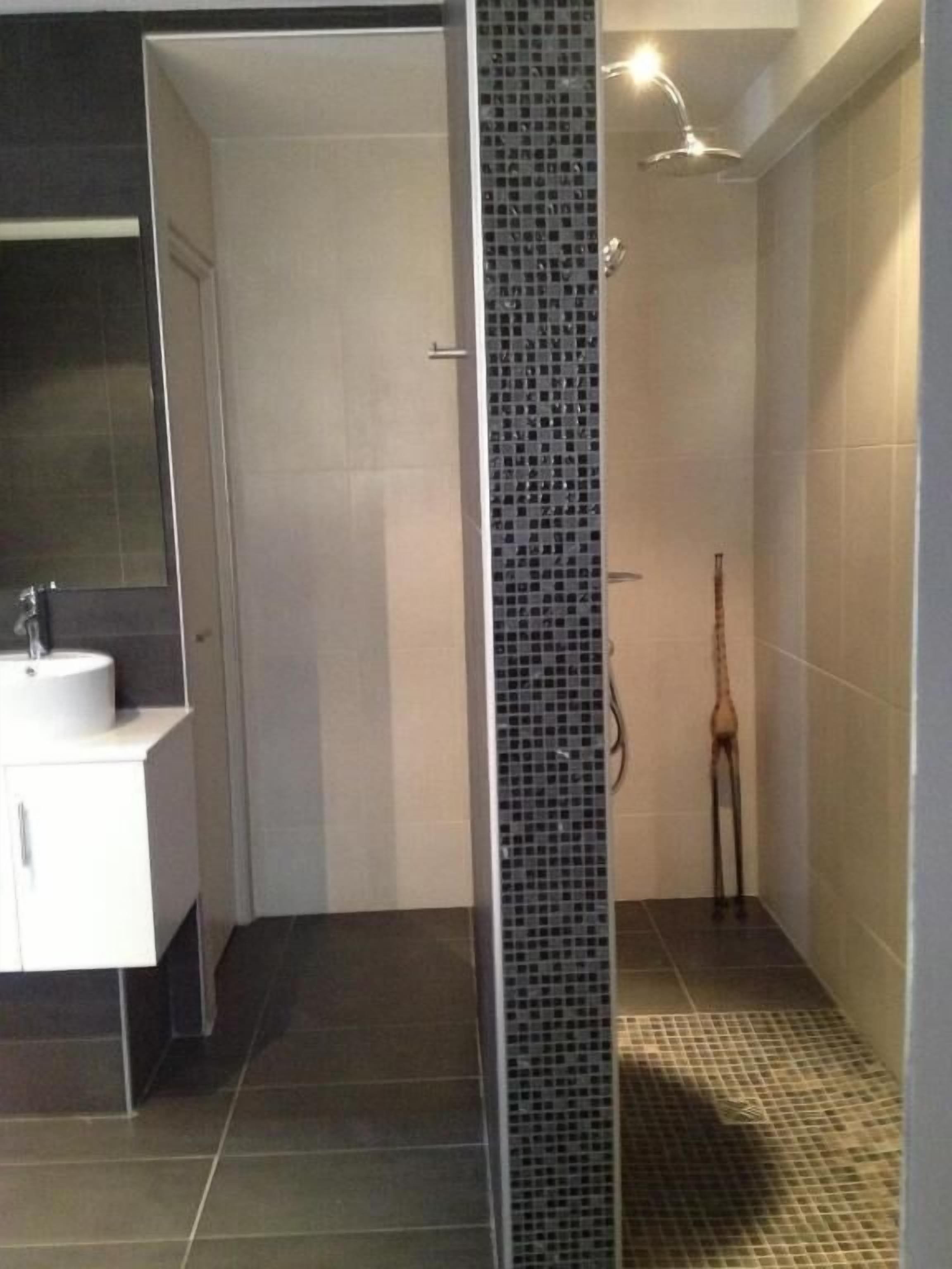 Casa de banho moderna com zona de duche, lavatório e chão em mosaico.