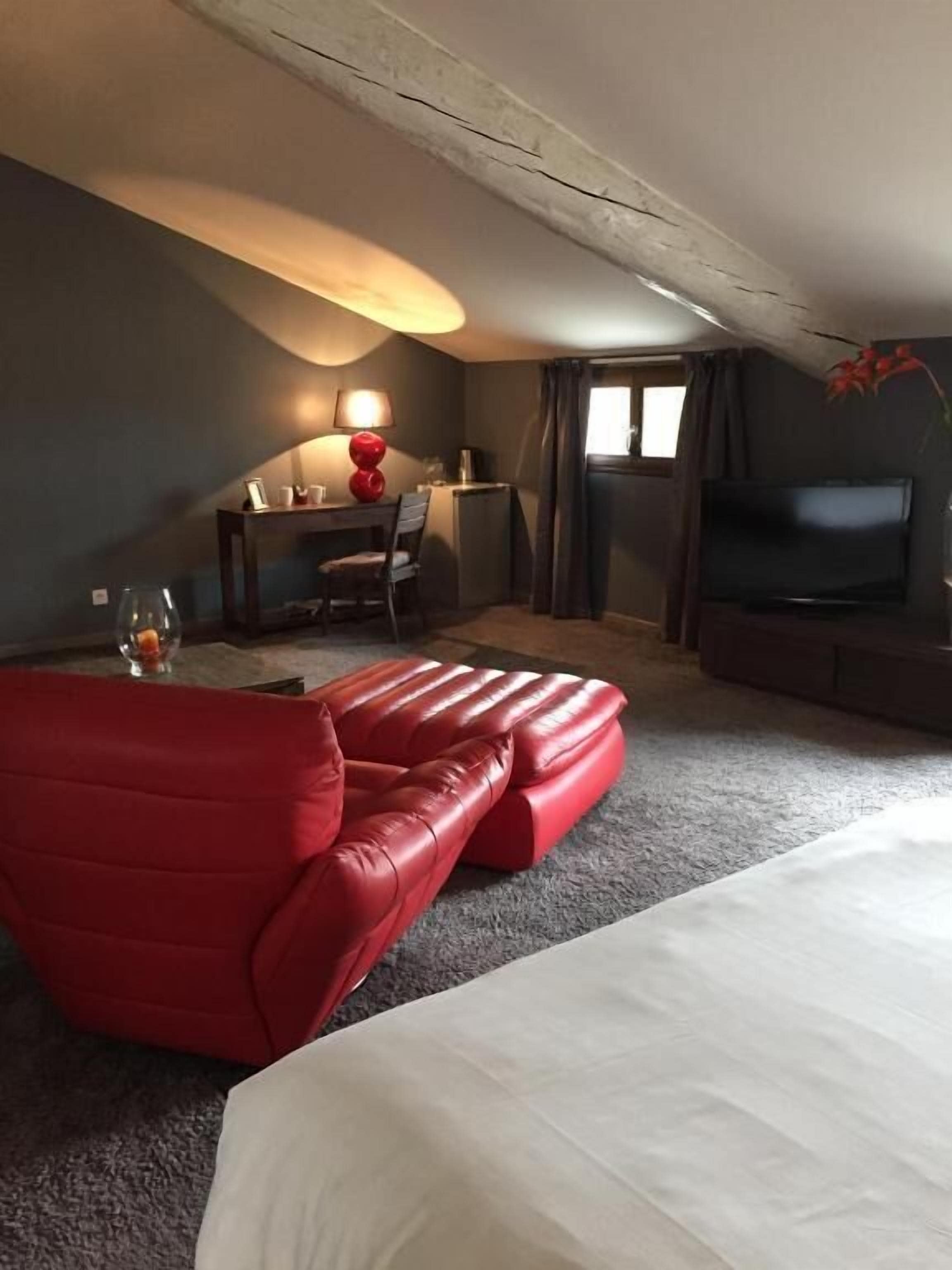 A hotel room with a large bed, a red sofa, a desk with a lamp, and a TV.