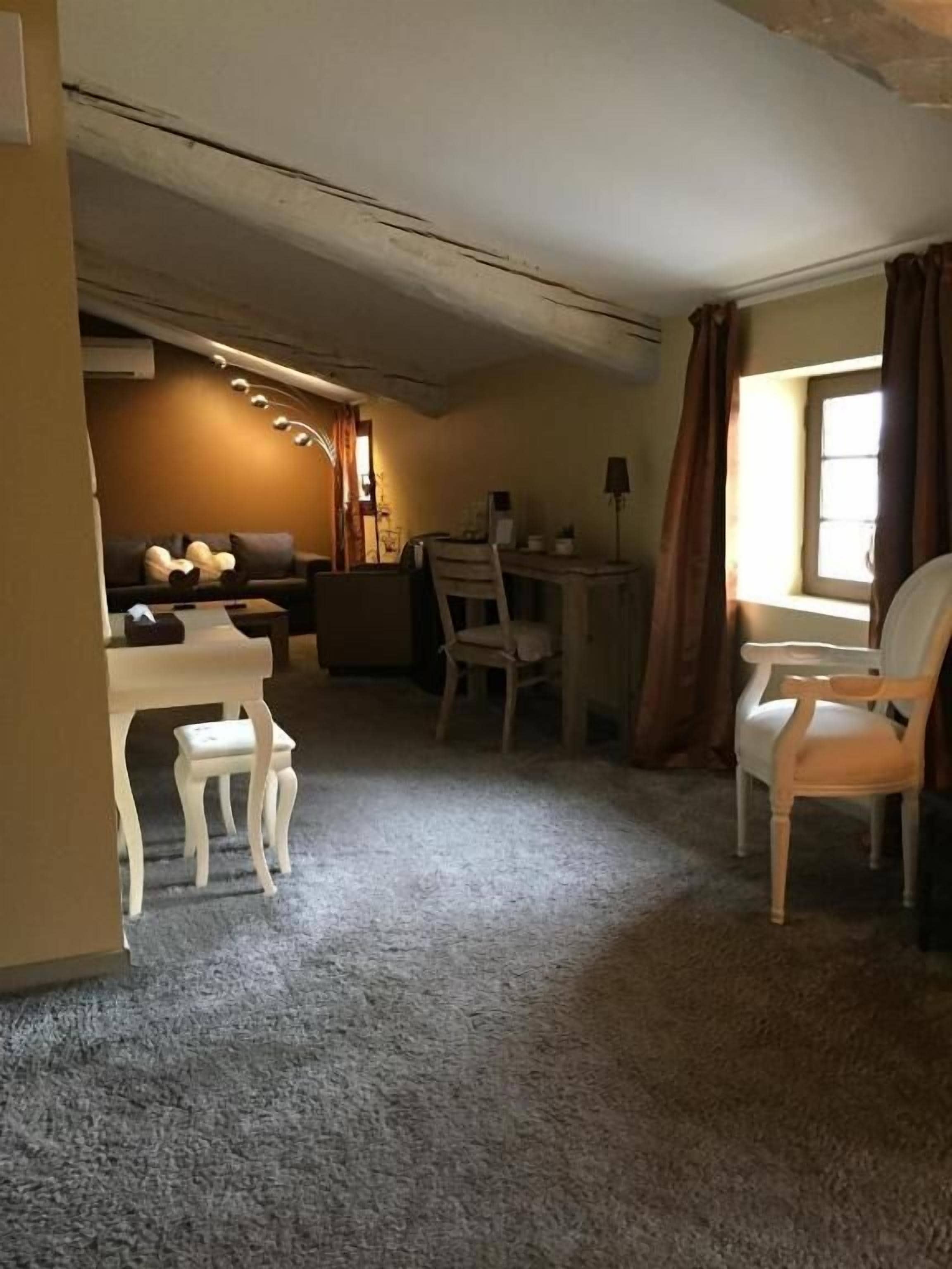 A room with a carpeted floor, a sofa, a dining table with chairs, and a window with curtains.