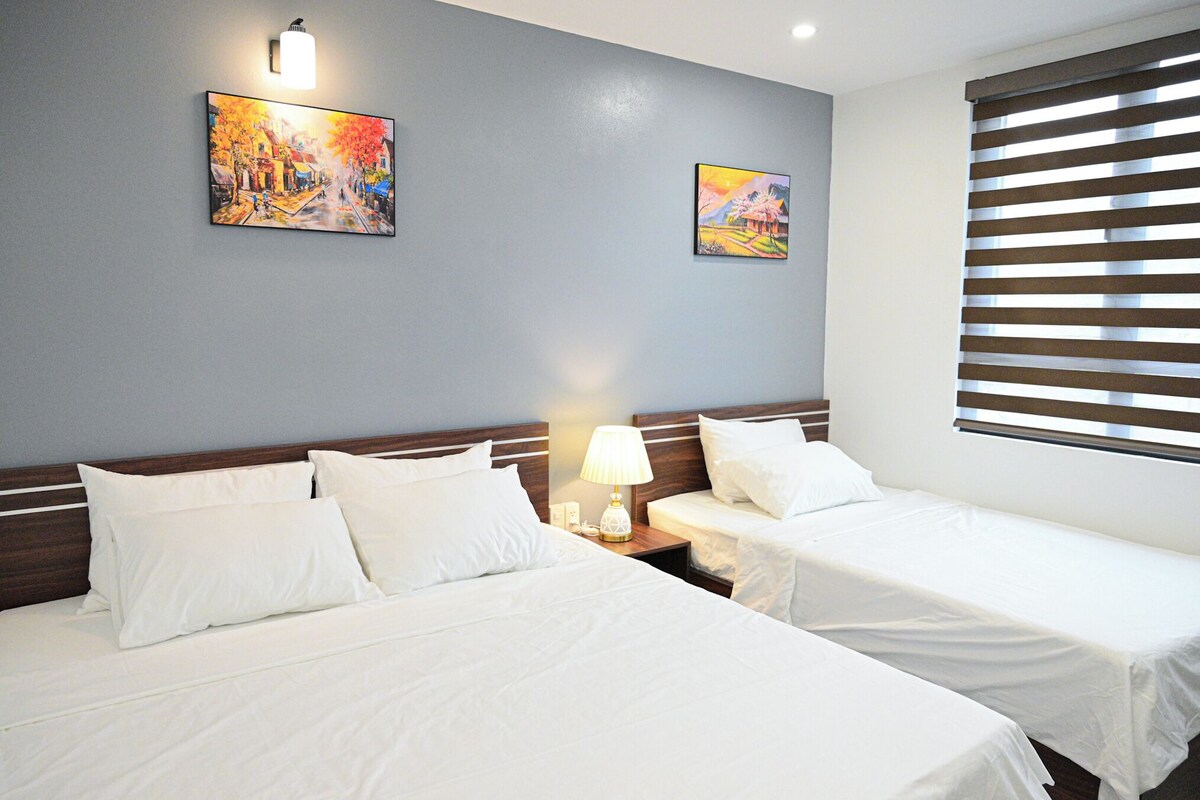 Habitación de hotel con dos camas, una mesita de noche con lámpara y dos cuadros en la pared.