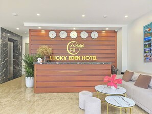 A reception desk with clocks, a logo, and a sign for Lucky Eden Hotel. - Lucky Eden Noi Bai Hotel (Hanoi)