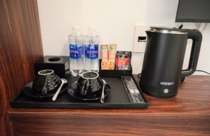 A hotel room's breakfast setup with a coffee maker, two water bottles, tea bags, and a tray with cups and spoons. - Lucky Eden Noi Bai Hotel (Hanoi)