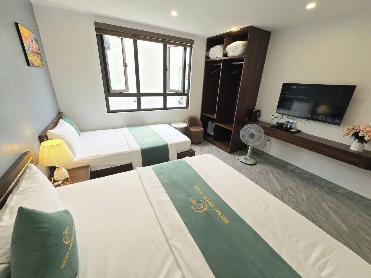 A hotel room with two beds, a wardrobe, a TV, and a fan.