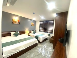 Quarto de hotel com duas camas, uma mesa pequena, televisão e obras de arte nas paredes.