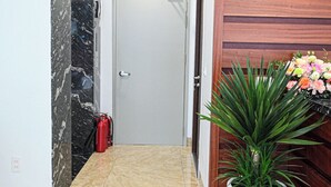 Un pasillo con piso de mármol, paneles de madera en la pared, una planta en maceta y un extintor.