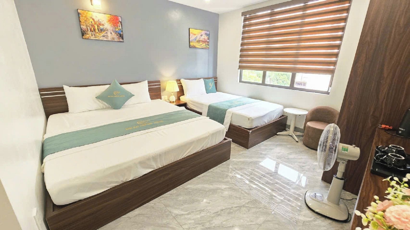 A hotel room with two beds, a sitting area, a fan, and artwork on the walls.