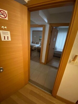 Ein Hotelzimmer mit Bett, Nachttisch und Fenster. Eine Tür mit einem Schild, das Rauchen verbietet.