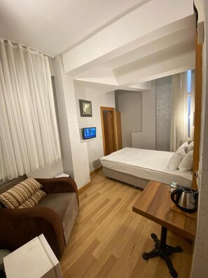 Een kleine kamer met een bed, een bureau, een stoel, een televisie en een raam met gordijnen.