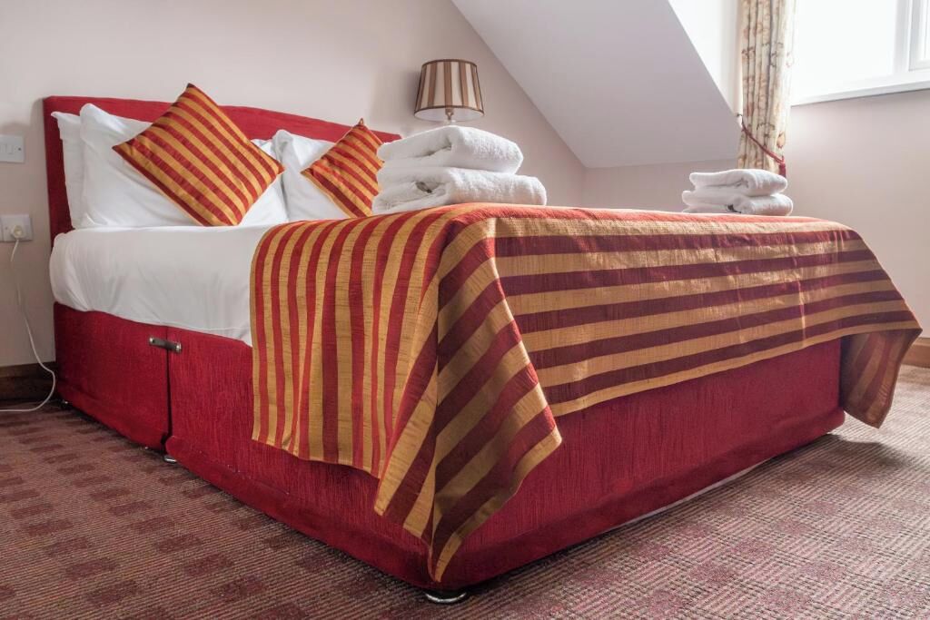Una habitación de hotel con una cama roja, ropa de cama a rayas y toallas sobre la cama.