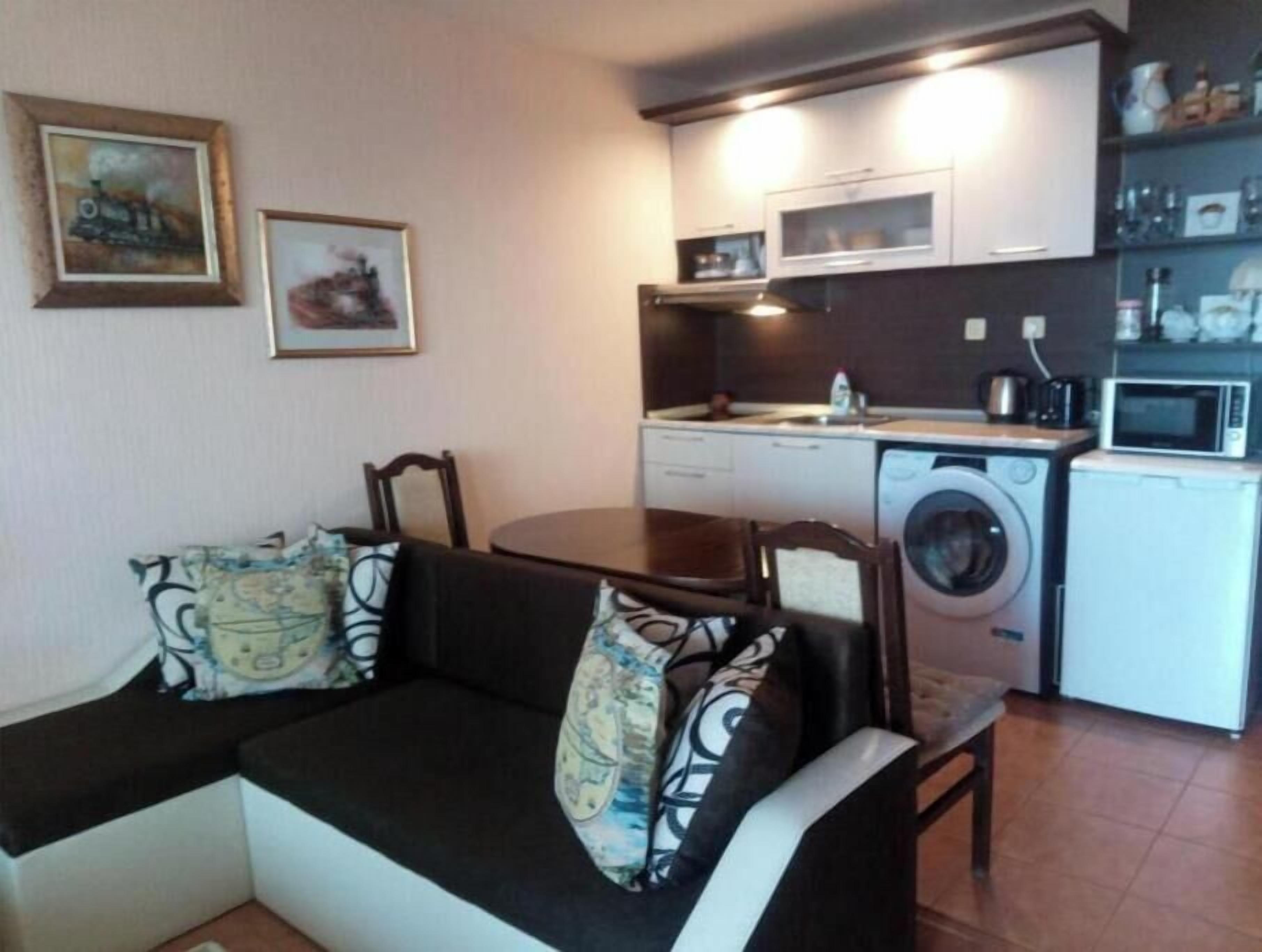 A compact living space with a sofa, a dining table, a washing machine, and a microwave.