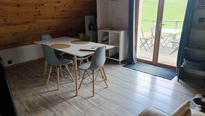 Interior de madeira com mesa de jantar, cadeiras, um sofá e vista para um campo verde através de uma porta de vidro.