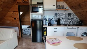 Cozinha compacta com micro-ondas, frigorífico e pia. Possui um espaço de refeições com mesa e cadeiras, e um pequeno espaço de estar com um sofá.