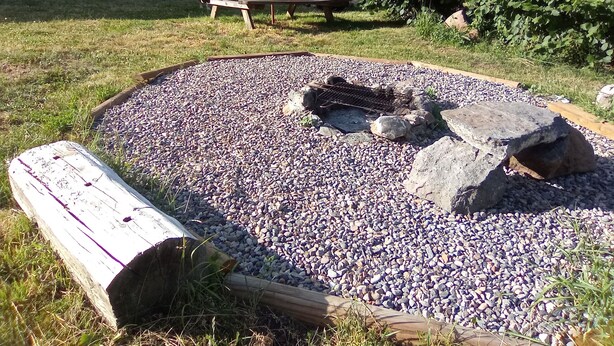 Uma área de jardim com lareira de cascalho, um banco de madeira e uma mesa de piquenique.