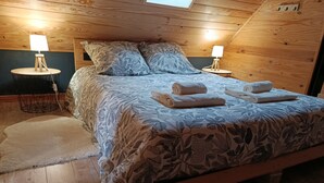 Um quarto aconchegante com teto de madeira, cama com roupa de flores, duas luminárias de cabeceira e toalhas dobradas.