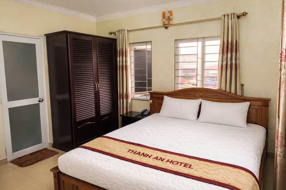 Quarto de hotel com uma cama, um guarda-roupa, uma janela com cortinas e uma porta.