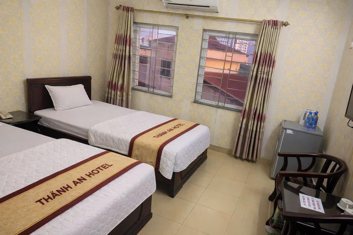 Quarto de hotel com duas camas, uma escrivaninha, uma cadeira e um pequeno armário.