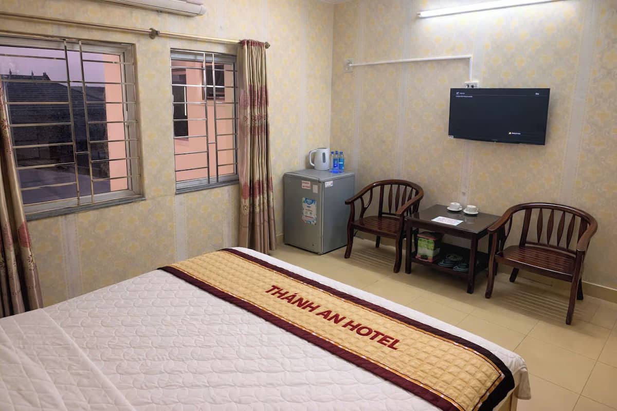 Quarto de hotel com cama, escrivaninha com duas cadeiras, televisão e um pequeno frigorífico.