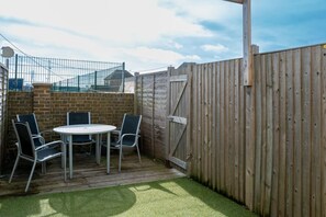 Un patio con una mesa y sillas, una valla de madera y un muro de ladrillo.