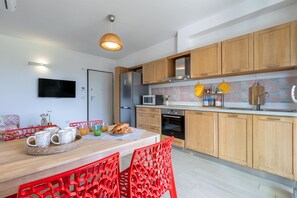 A modern kitchen with wooden cabinets, a microwave, and a dining area with red chairs. - Casa Eolo. Appartamento con terrazza e box privato. (Alghero)