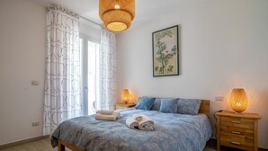 Un dormitorio con cama, dos lámparas de noche, una mesita de noche de madera, un tapete verde y una obra de arte colgada en la pared.