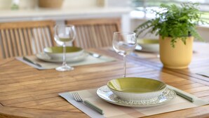 Una mesa de comedor con un tazón verde, dos copas de vino y un florero amarillo con una planta.