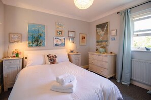 A bedroom with a bed, bedside tables, a dresser, and artwork on the walls. - Stylish 3-Bed Home | Garden, Parking & Near Quay (Kent)