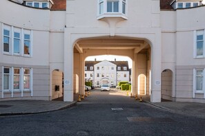 A building entrance with a large archway, a paved driveway, and a white car parked in the distance. - Stylish 3-Bed Home | Garden, Parking & Near Quay (Kent)