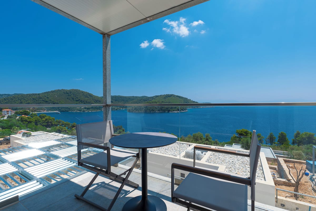 A balcony with a table and chairs overlooking a body of water and hills.