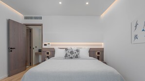 A modern bedroom with a large bed, a wooden wardrobe, a bedside table, and a wall-mounted light fixture. - Adrina Grand Hotel (Skopelos)
