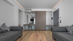 A modern hotel room with two grey sofas, a wooden floor, a TV, and a wardrobe. - Adrina Grand Hotel (Skopelos)