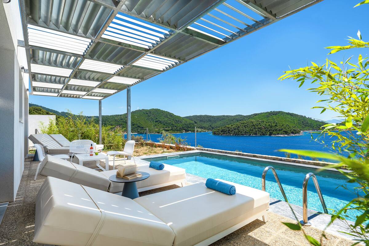 A poolside area with lounge chairs, a table, and a view of the sea.