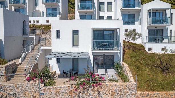 A modern multi-story building with balconies, outdoor seating, and a stone pathway. - Adrina Grand Hotel (Skopelos)