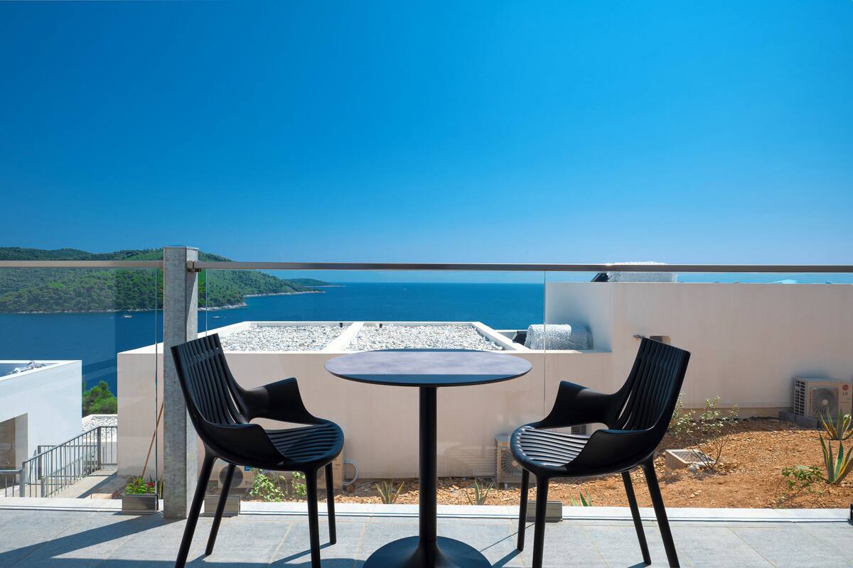 A terrace with two chairs and a table, overlooking a body of water and hills.
