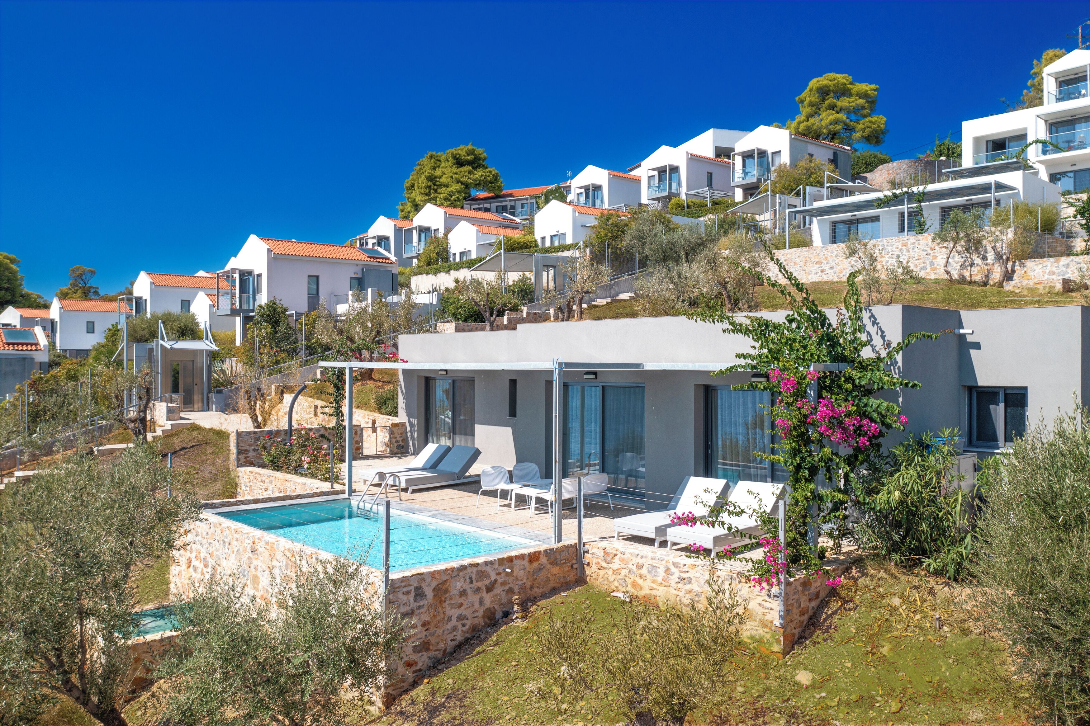 A hillside residential area with modern houses, a swimming pool, and outdoor seating.