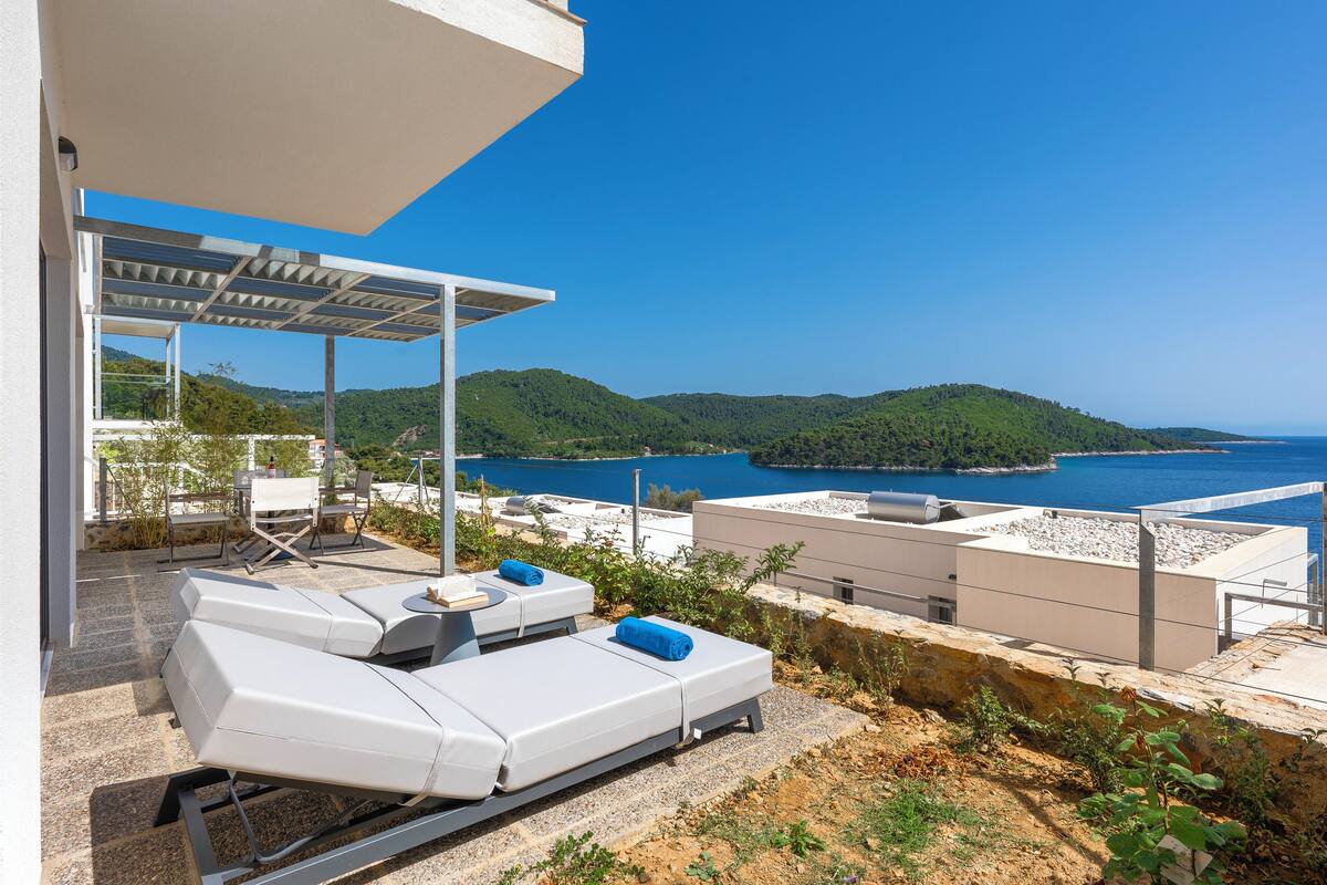 A rooftop terrace with lounge chairs, a pergola, and a view of the sea and hills.