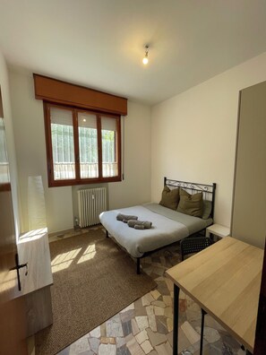A bedroom with a bed, a radiator, a window with blinds, a desk, and a chair. - Gabri House (Speranza)
