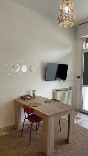 Ein Essbereich mit Holztisch, roten Stühlen, einer gewebten Pendelleuchte, einem an der Wand montierten Fernseher und einer Heizung.