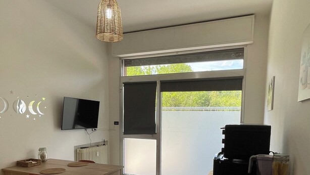 Ein moderner Wohnraum mit Essbereich, einem an der Wand montierten Fernseher, einem großen Fenster und einer Deckenleuchte.