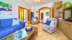 A living room with a sofa, armchair, and coffee table, wooden cabinets, and a painting on the wall. - Apartment Bijenica - surrounded by lush greenery (Vrbnik)