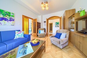 Ein Wohnzimmer mit Sofa, Sessel und Couchtisch, Holzkredenz und einem Gemälde an der Wand.