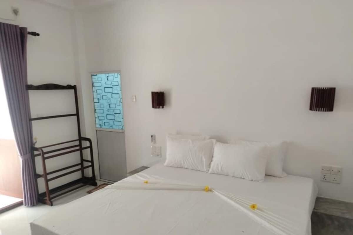 Habitación de hotel con una cama, una ventana con diseño geométrico, una lámpara de pared y un enchufe.