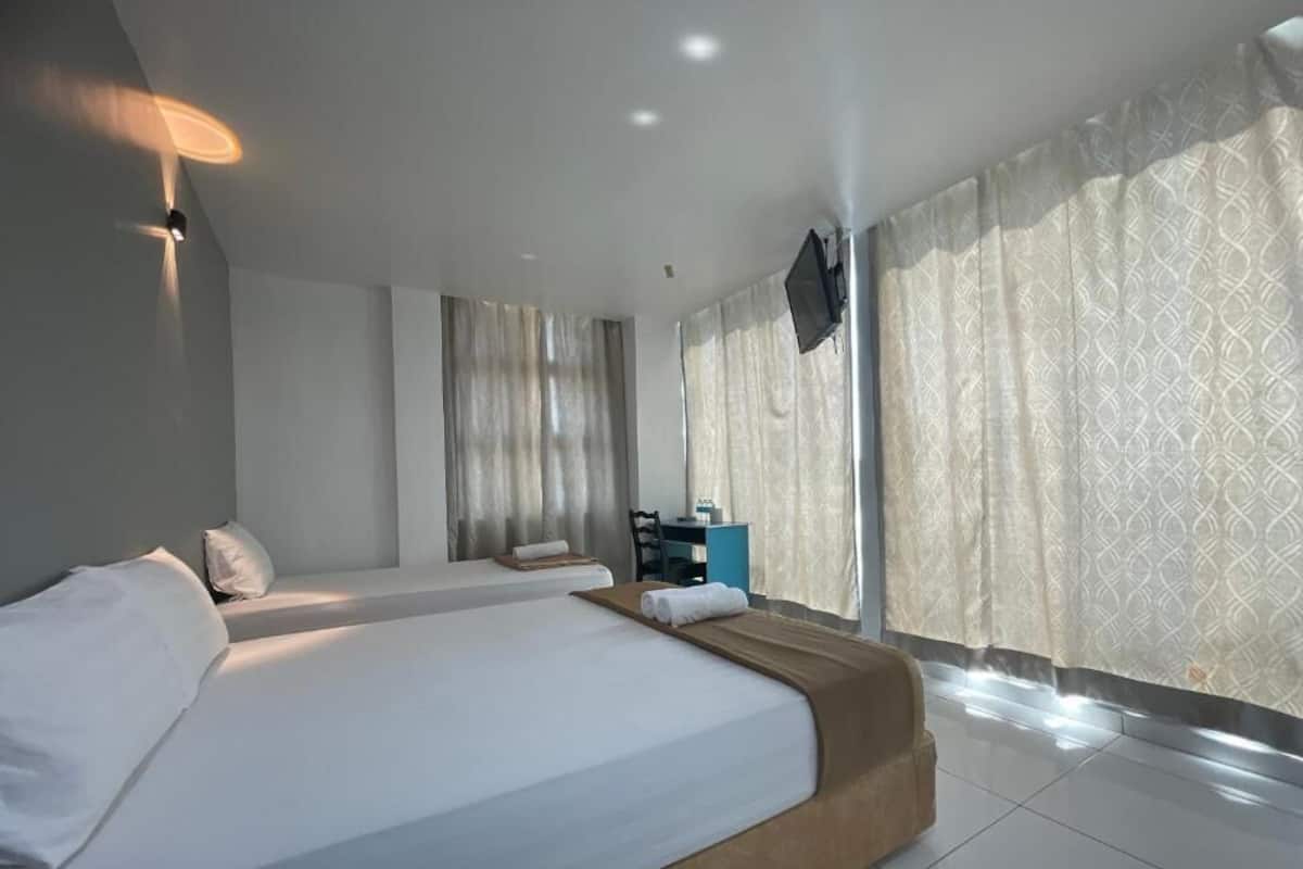 Habitación de hotel con una cama grande, un escritorio, una silla, un televisor montado en la pared y una ventana con cortinas.
