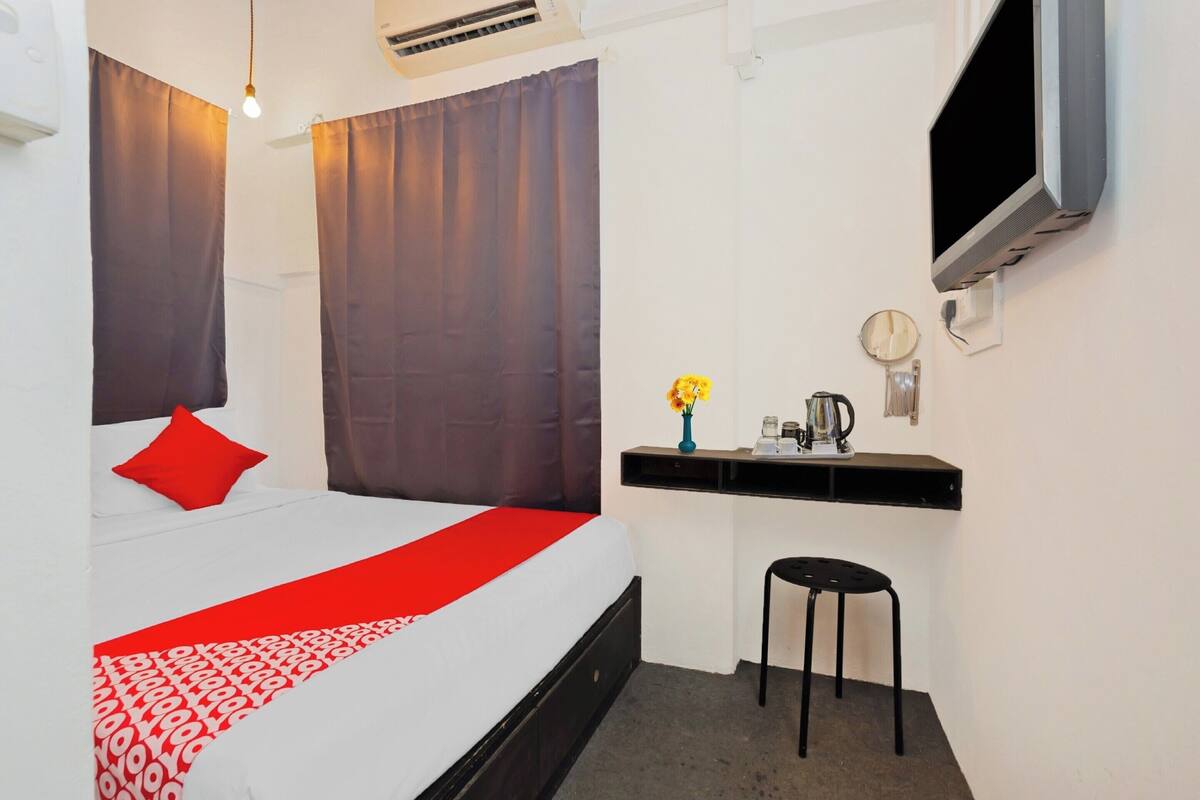 Una habitación de hotel con una cama, un escritorio, una silla, un televisor y una pequeña mesa con un florero.
